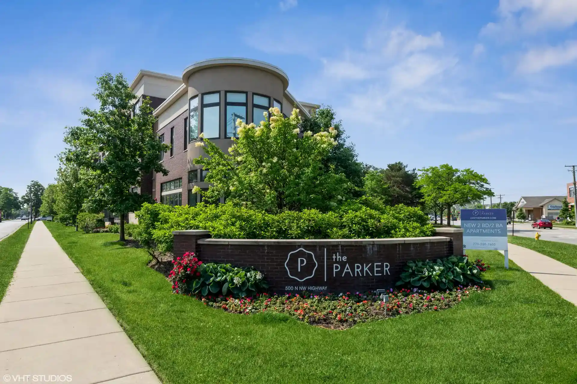 The Parker front red brick sign in front of bushes, trees, and with sidewalks running down both sides.